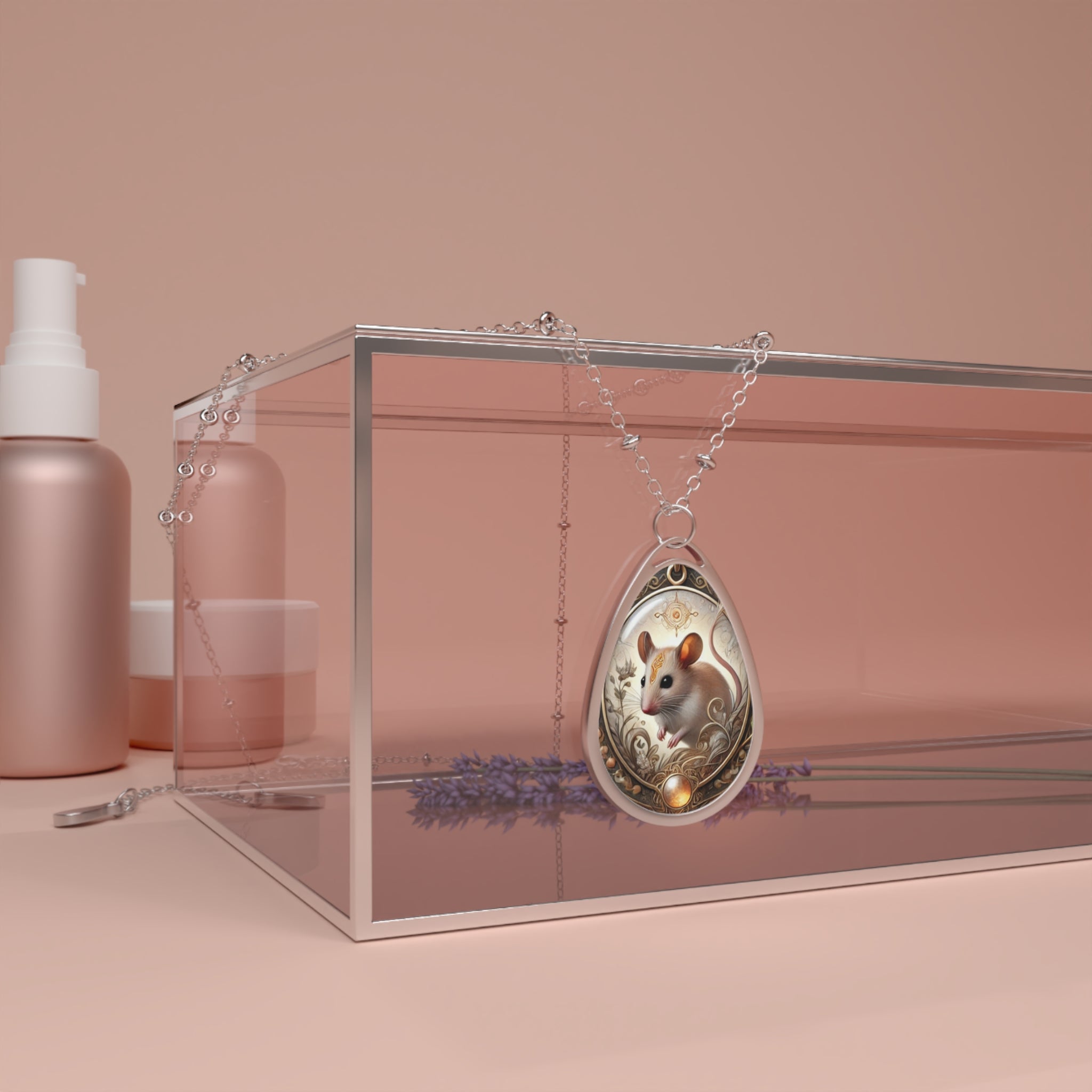 A silver teardrop pendant with an intricately detailed mouse illustration, elegantly draped over a clear glass box with soft pink and lavender decor in the background. The pendant’s ornate gold filigree and earthy colors give it a vintage, enchanting look.