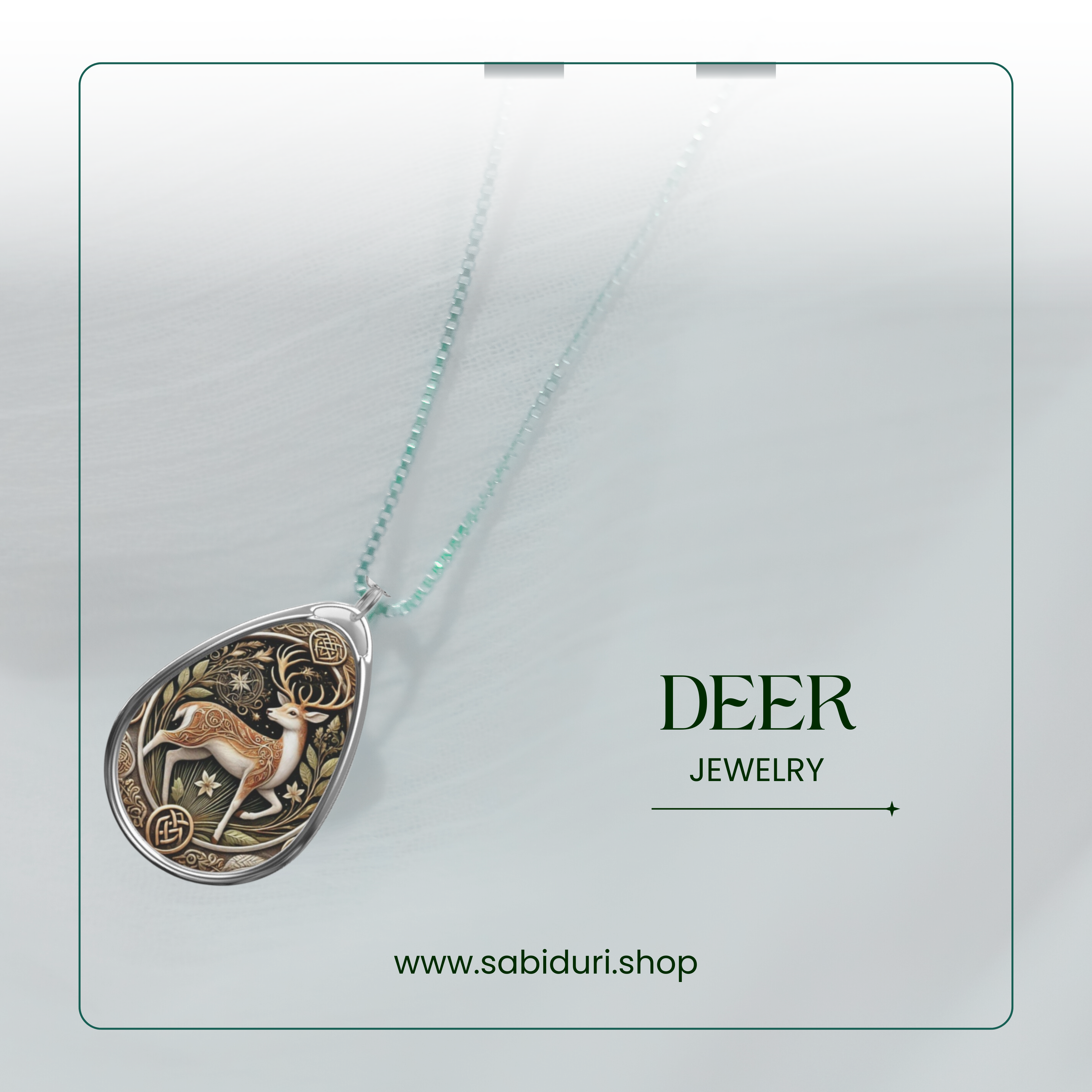 A silver teardrop pendant featuring a detailed illustration of a deer with antlers, embellished with floral motifs. The necklace is displayed on a light, textured surface, accompanied by the text "DEER JEWELRY" and the website URL "www.sabiduri.shop."