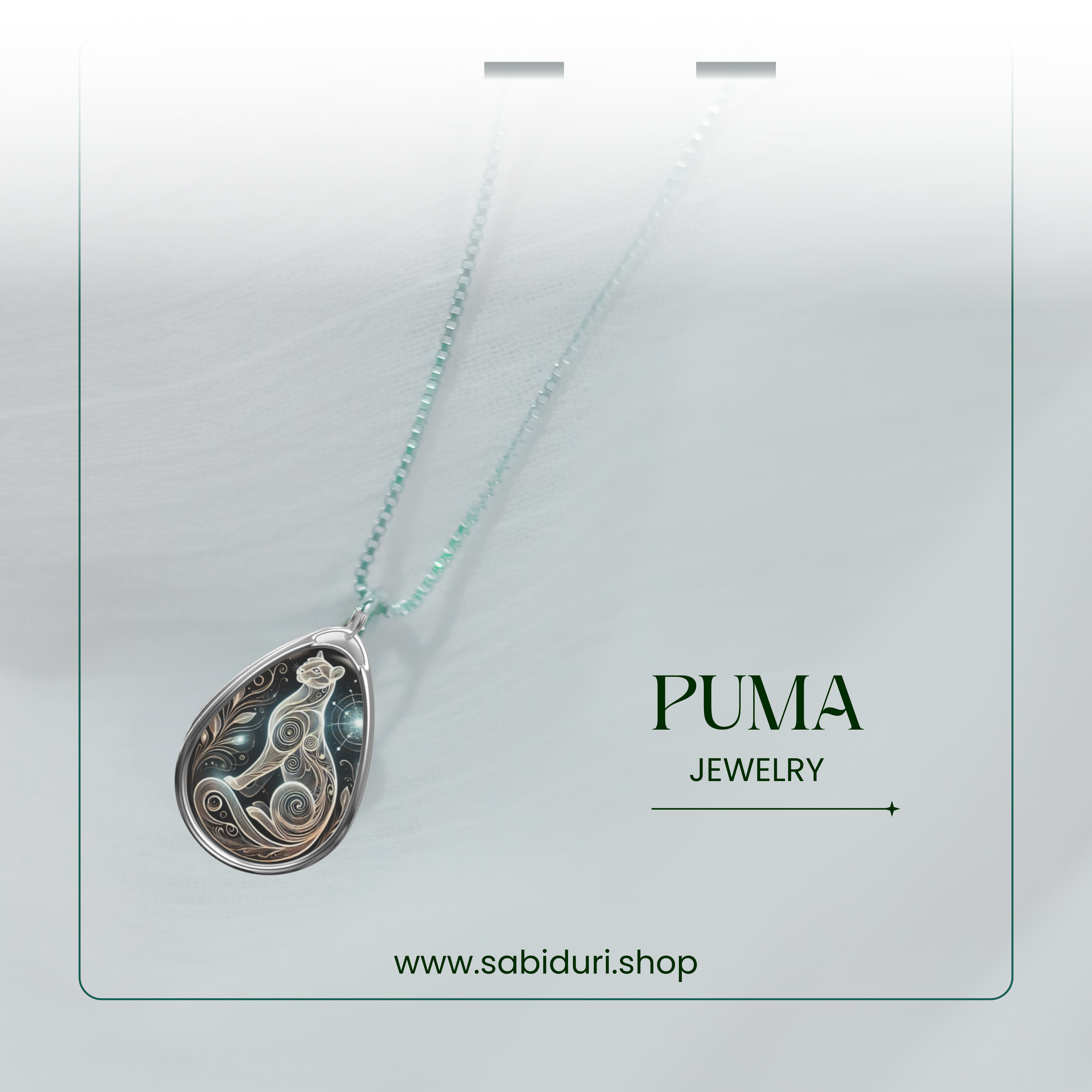 A close-up of a puma-themed pendant necklace, suspended on a delicate chain against a soft, blurred white fabric. The pendant features a mystical swirling puma design with celestial details. The text "PUMA JEWELRY" and "www.sabiduri.shop" is elegantly placed.