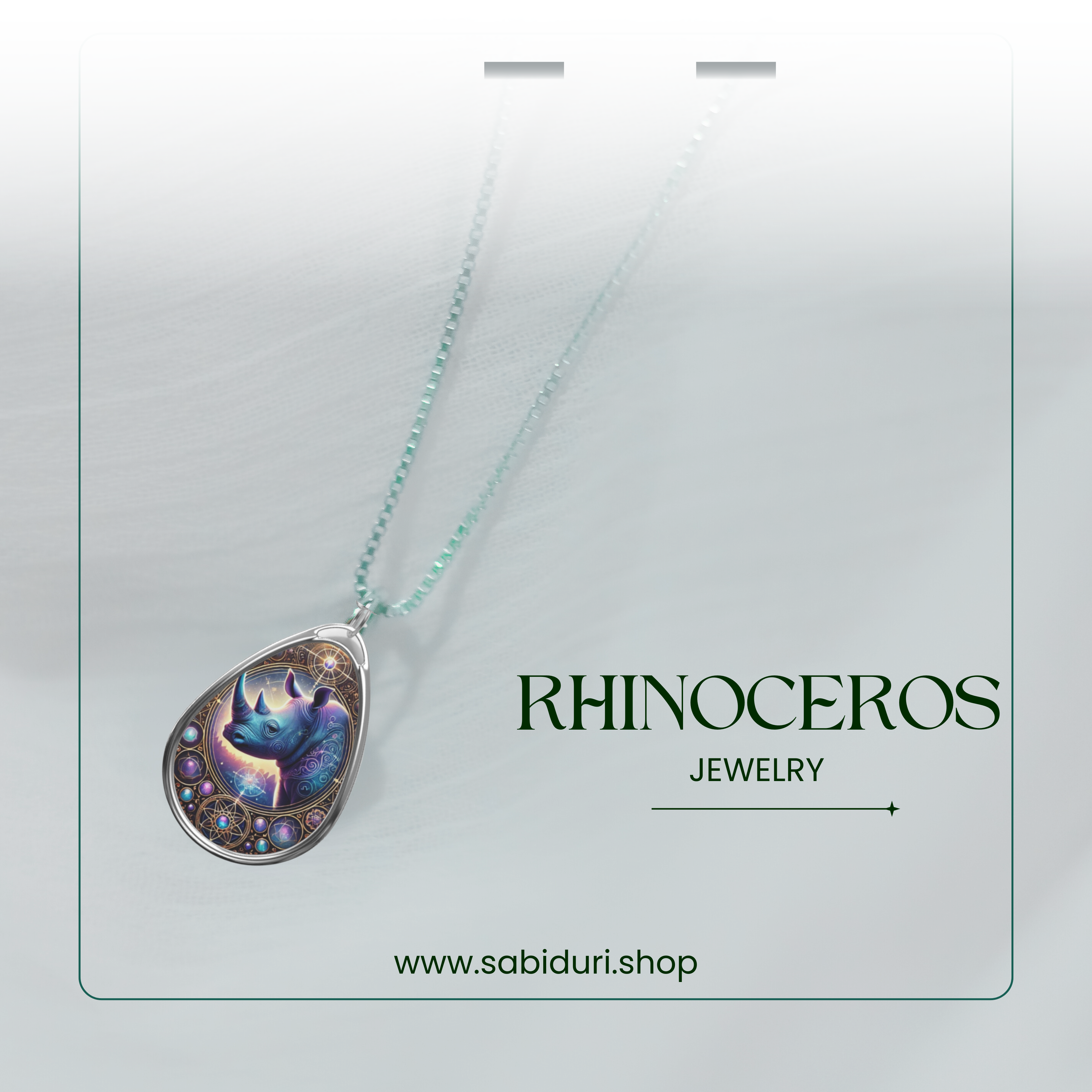 A silver rhinoceros pendant necklace with an ethereal purple and blue design, displayed against a soft white fabric background. The chain is beaded with a subtle gradient, and "Rhinoceros Jewelry" along with the website URL is elegantly placed in the design.