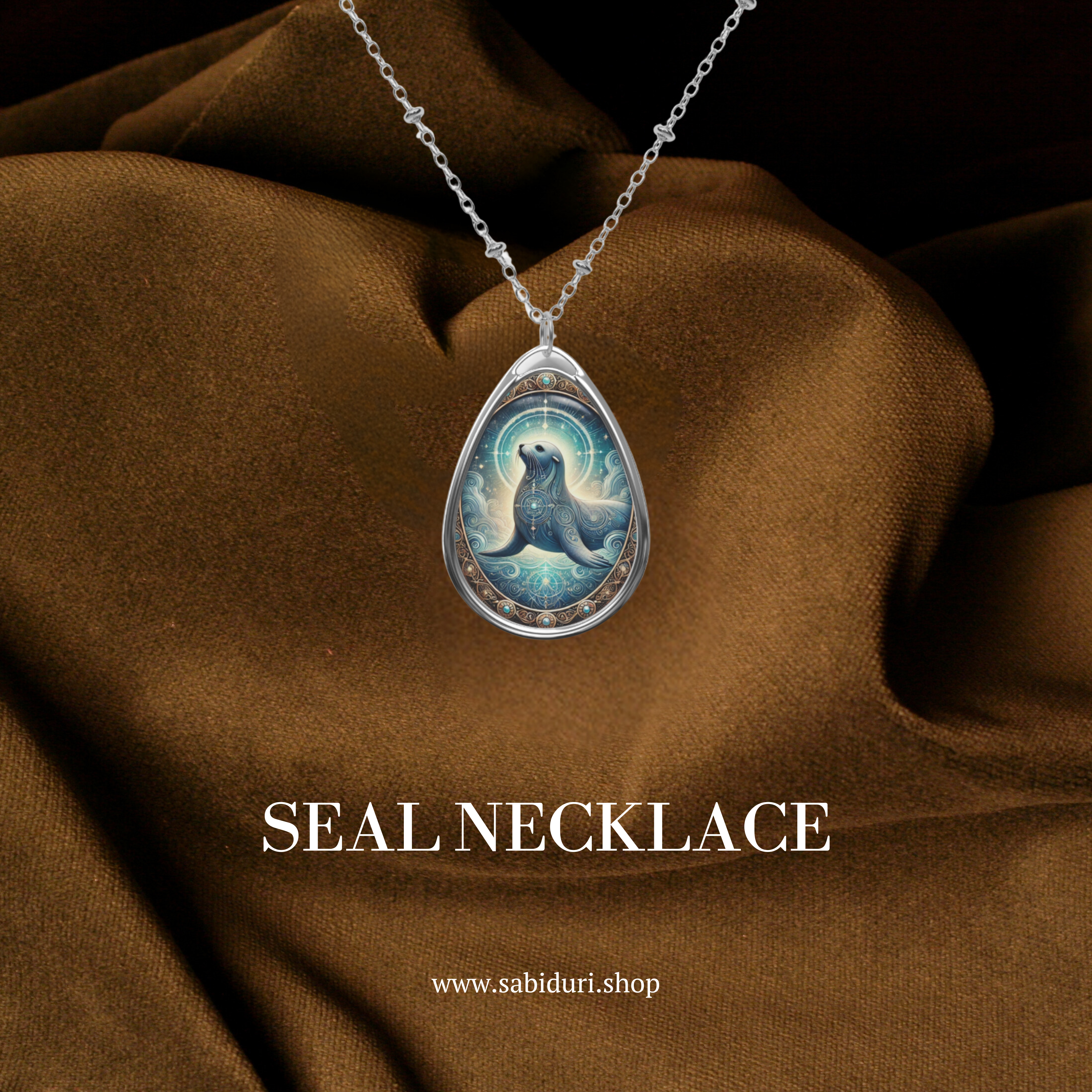 A teardrop-shaped silver necklace featuring an intricately designed seal pendant, set against a luxurious brown fabric background. The pendant displays a detailed seal illustration with glowing accents and oceanic swirls. The text "SEAL NECKLACE" and "www.sabiduri.shop" is displayed in the image.