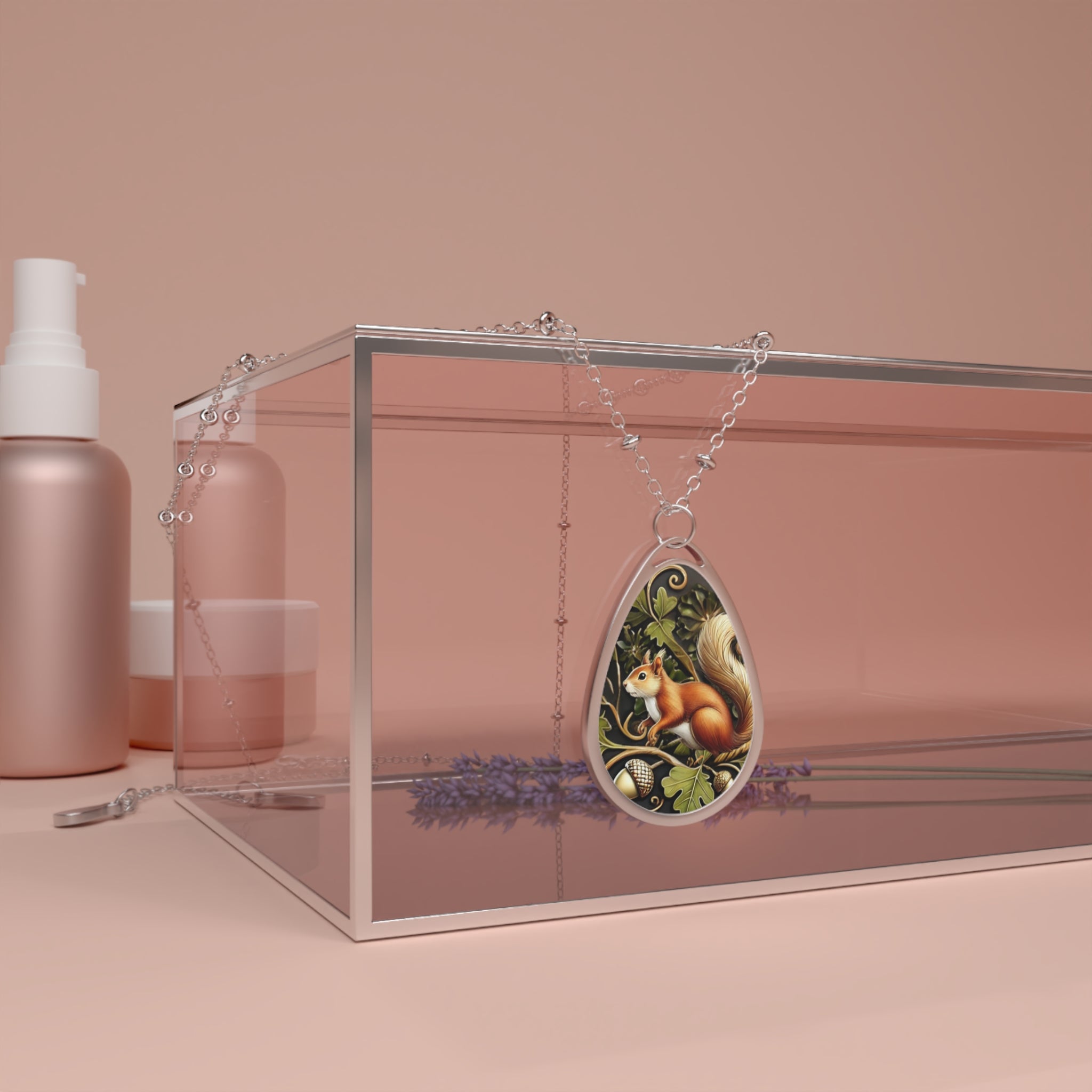 A teardrop-shaped pendant necklace with a squirrel illustration, featuring acorns and oak leaves, draped over the edge of a clear glass box. The background includes soft pink cosmetic bottles and sprigs of lavender.