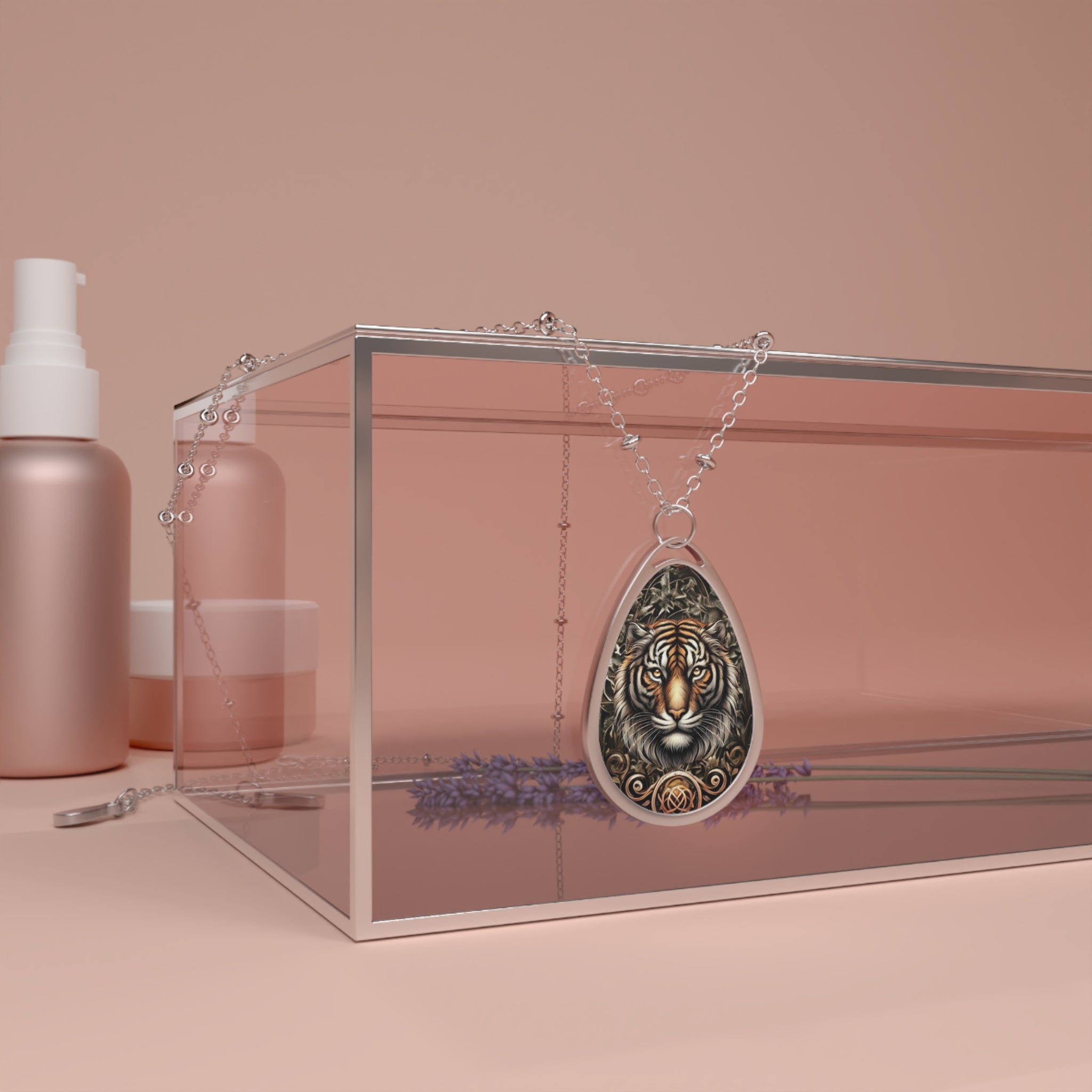 A silver necklace with a teardrop-shaped pendant featuring an intricate tiger design, draped over a clear, pink-tinted glass box. The background includes rose-gold cosmetic bottles and a sprig of lavender, creating a luxurious, soft ambiance.