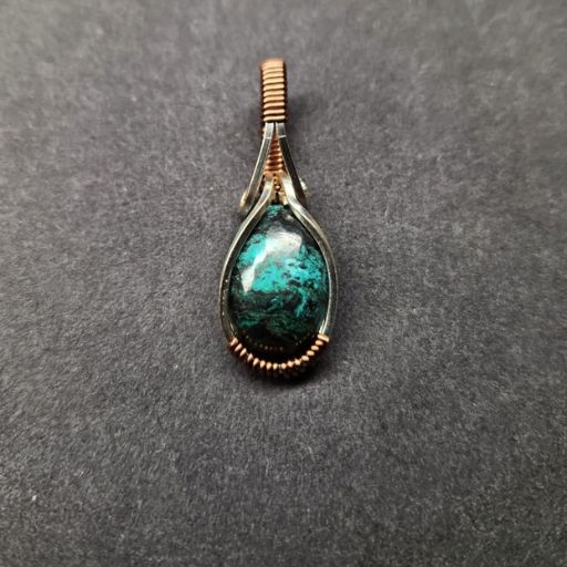 A simple yet striking pendant showcasing a teardrop-shaped, vibrant turquoise stone set within a copper wire frame, presented against a grey backdrop.