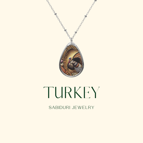 A close-up of a silver necklace pendant featuring a beautifully designed turkey with its feathers fanned out and surrounded by decorative elements. The background is a plain cream color with the text "TURKEY Sabiduri Jewelry."