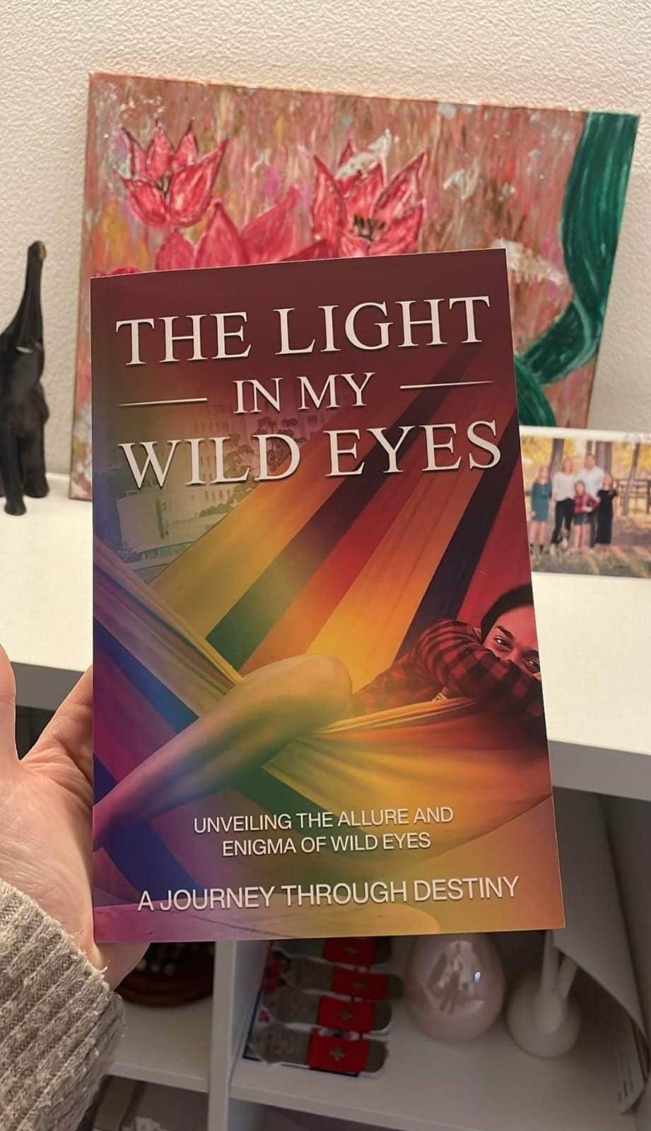 A hand holds 'The Light in My Wild Eyes' book with a colorful cover, suggestive of a vibrant and transformative narrative within its pages.