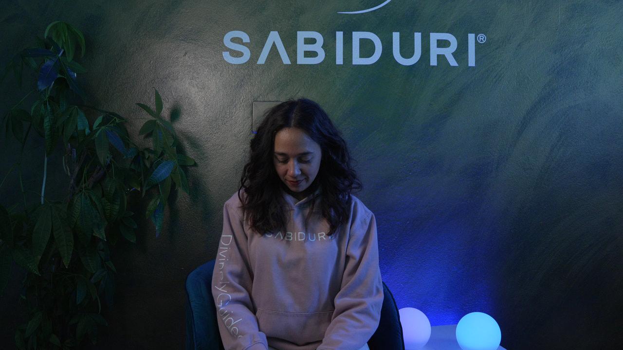 Woman sitting in front of a dark background with 'SABIDURI' branding.