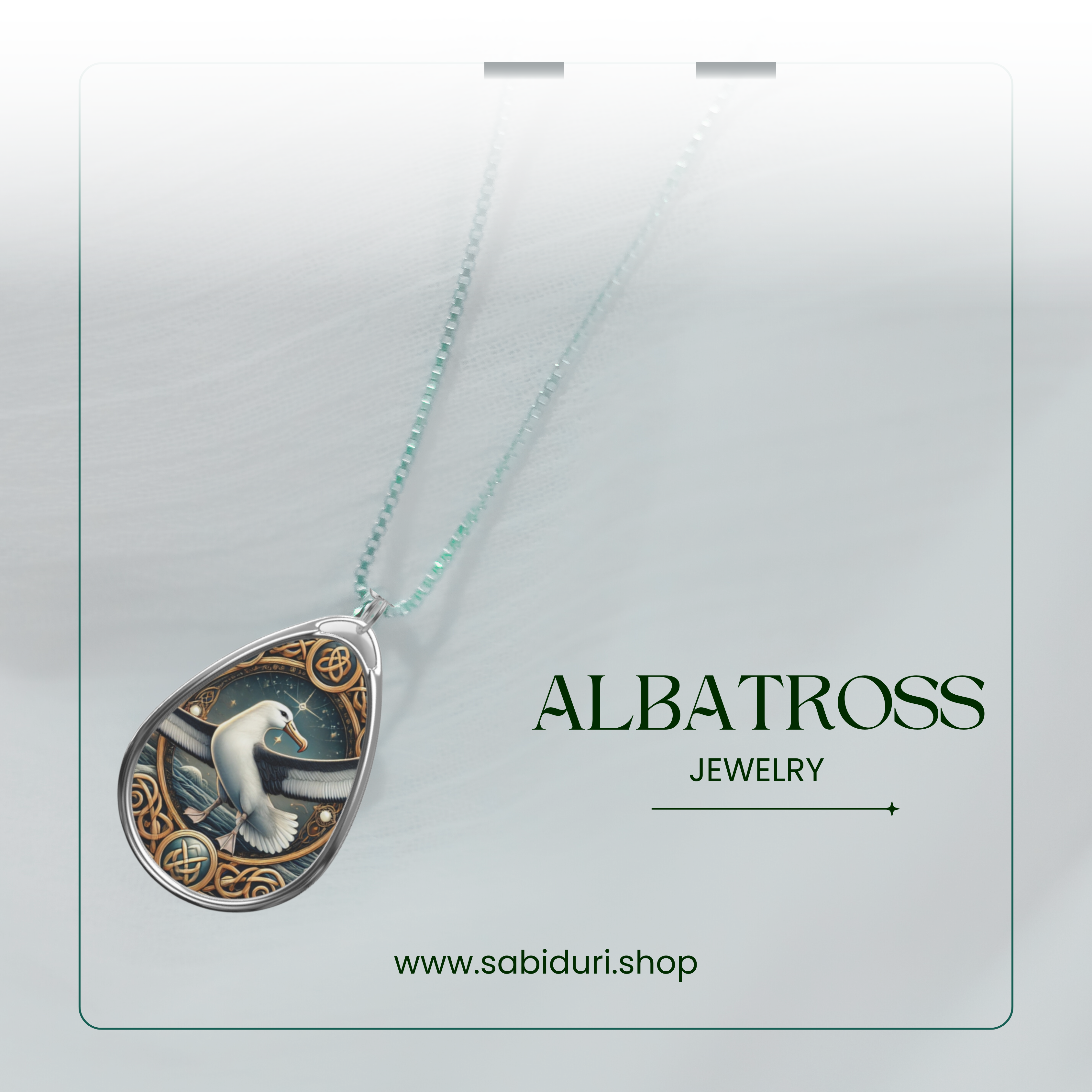 A close-up of a silver albatross pendant necklace, featuring a maritime-themed design with swirling wave patterns and golden accents. The pendant rests on a soft white fabric background, with the words "ALBATROSS JEWELRY" and the website "www.sabiduri.shop" in an elegant green font.