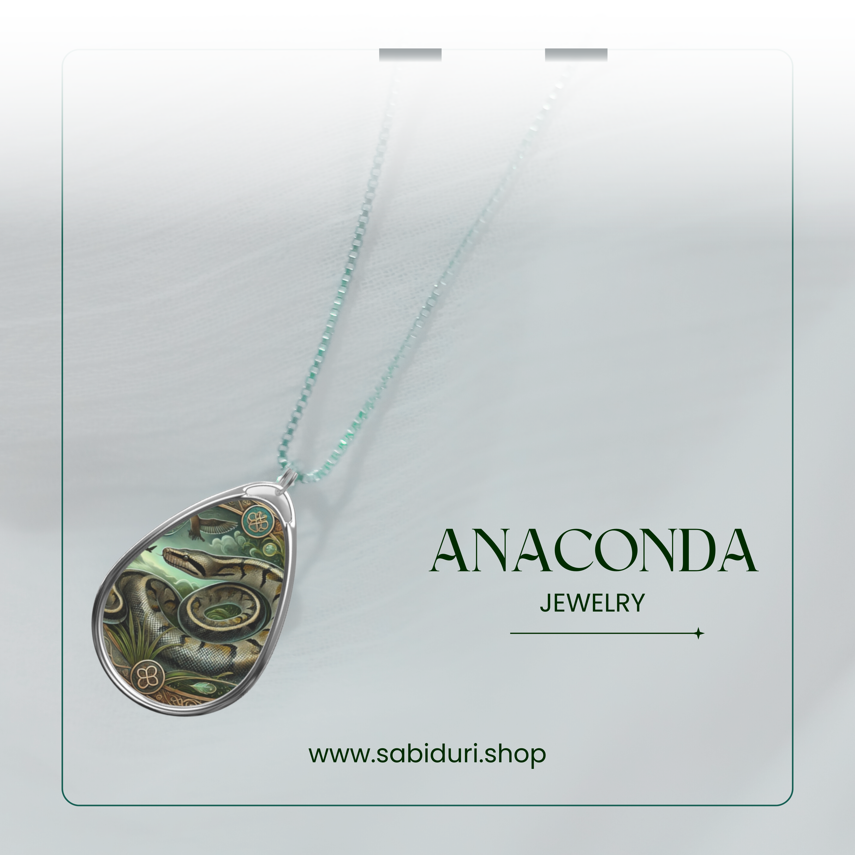 A close-up of a silver anaconda pendant necklace, featuring an elaborate rainforest-inspired design with swirling patterns and green gemstone accents. The pendant rests on a soft white fabric background, with the words "ANACONDA JEWELRY" and the website "www.sabiduri.shop" in an elegant green font.