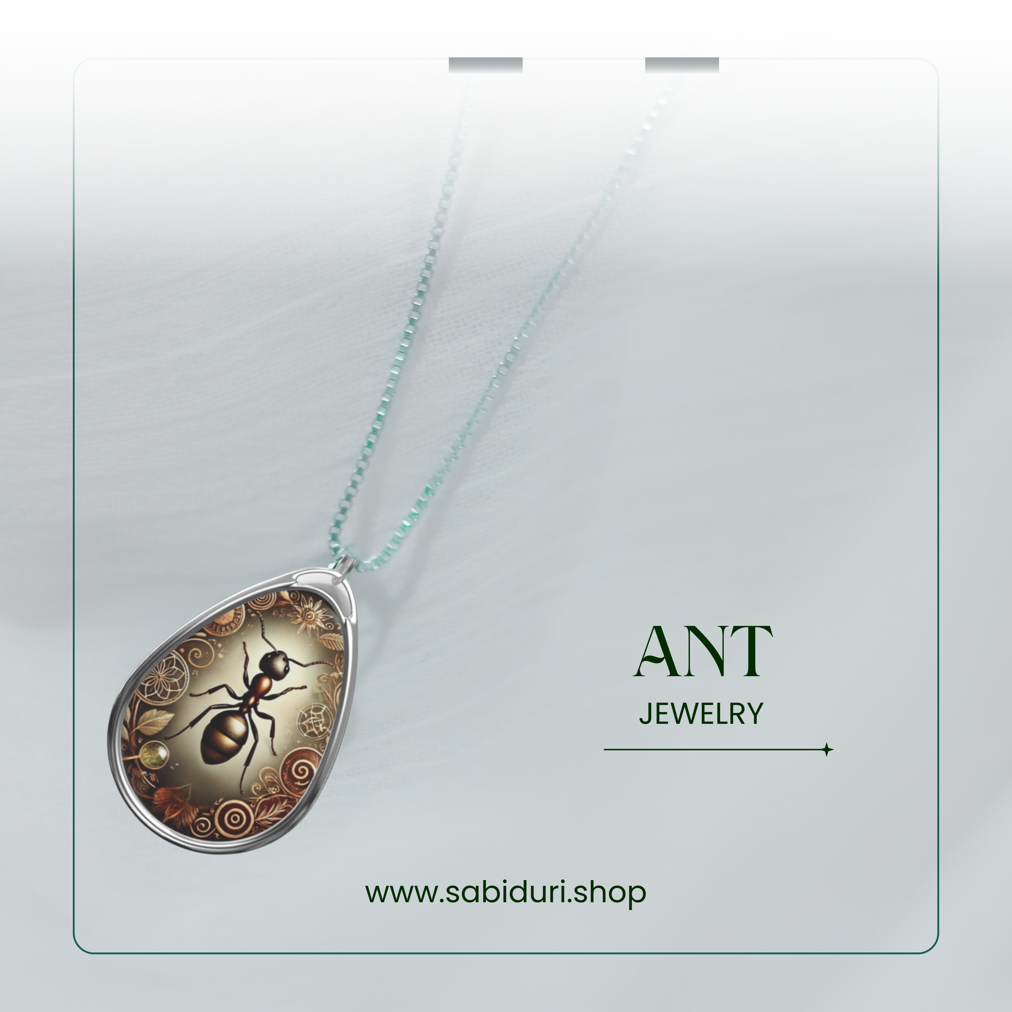 A close-up of a silver ant pendant necklace, featuring an elaborate design with swirling patterns and golden accents. The pendant rests on a soft white fabric background, with the words "ANT JEWELRY" and the website "www.sabiduri.shop" in an elegant green font.