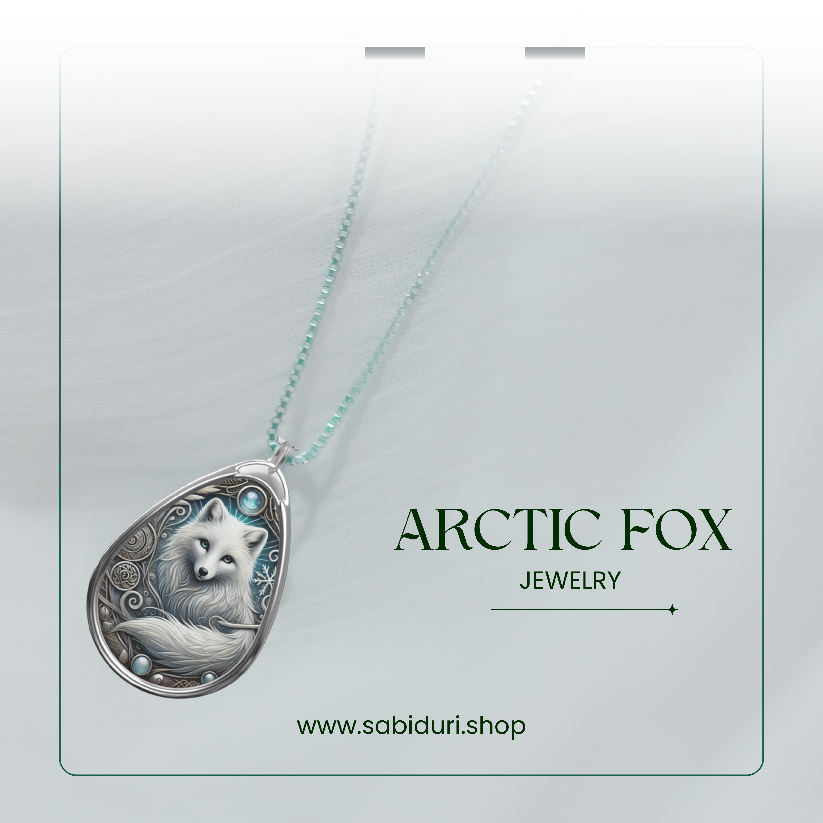 A close-up of a silver Arctic fox pendant necklace, featuring an intricate winter-themed design with swirling patterns and icy blue accents. The pendant rests on a soft white fabric background, with the words "ARCTIC FOX JEWELRY" and the website "www.sabiduri.shop" in a refined green font.