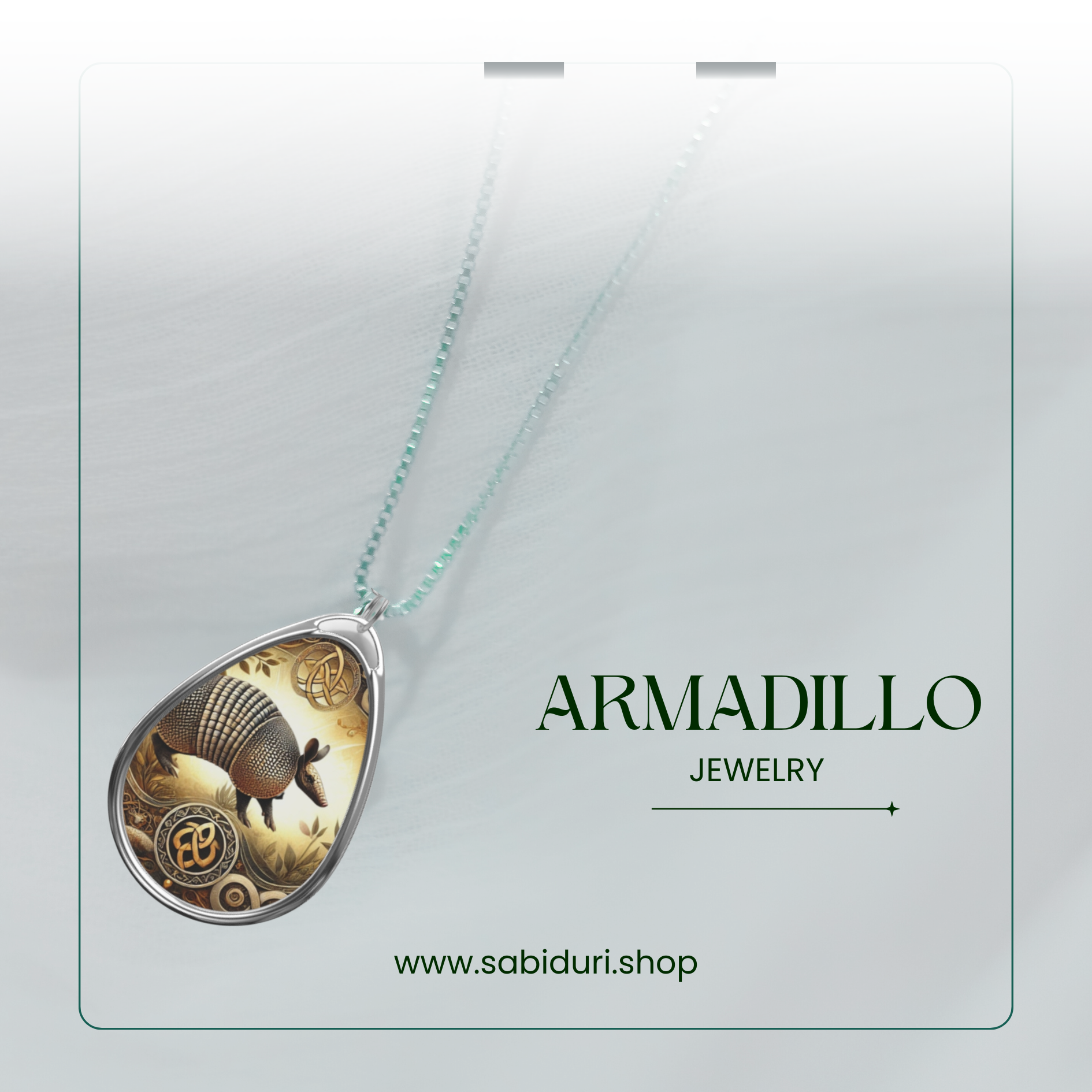 A close-up of a silver armadillo pendant necklace, featuring a nature-inspired design with intricate details and a golden-hued background. The pendant rests on a soft white fabric backdrop, with the words "ARMADILLO JEWELRY" and the website "www.sabiduri.shop" in an elegant green font.