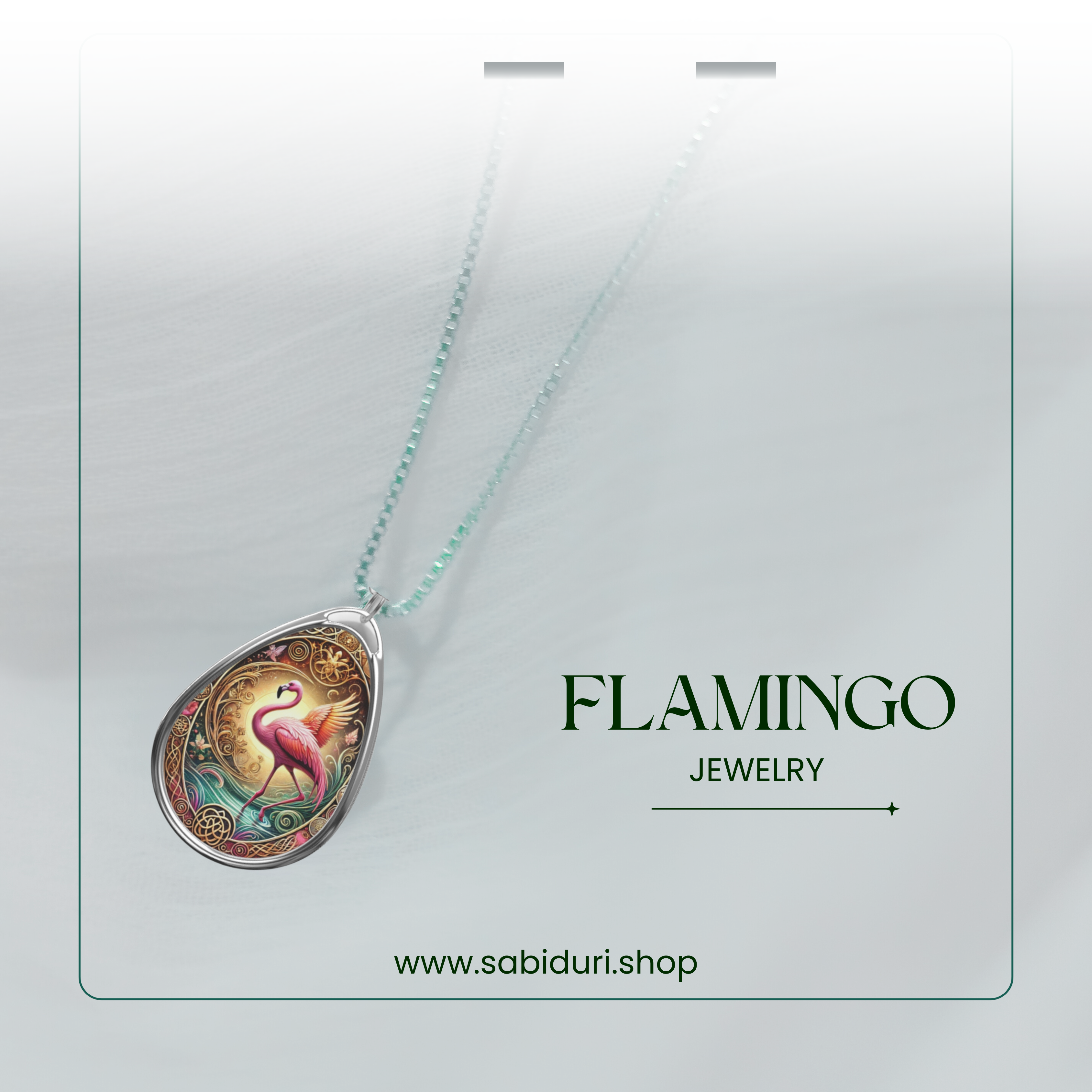 The flamingo necklace displayed against a soft, airy white fabric with a subtle gradient. The pendant glows with vibrant pink, teal, and gold hues, emphasizing the intricate detailing. "FLAMINGO JEWELRY" and "www.sabiduri.shop" appear below.