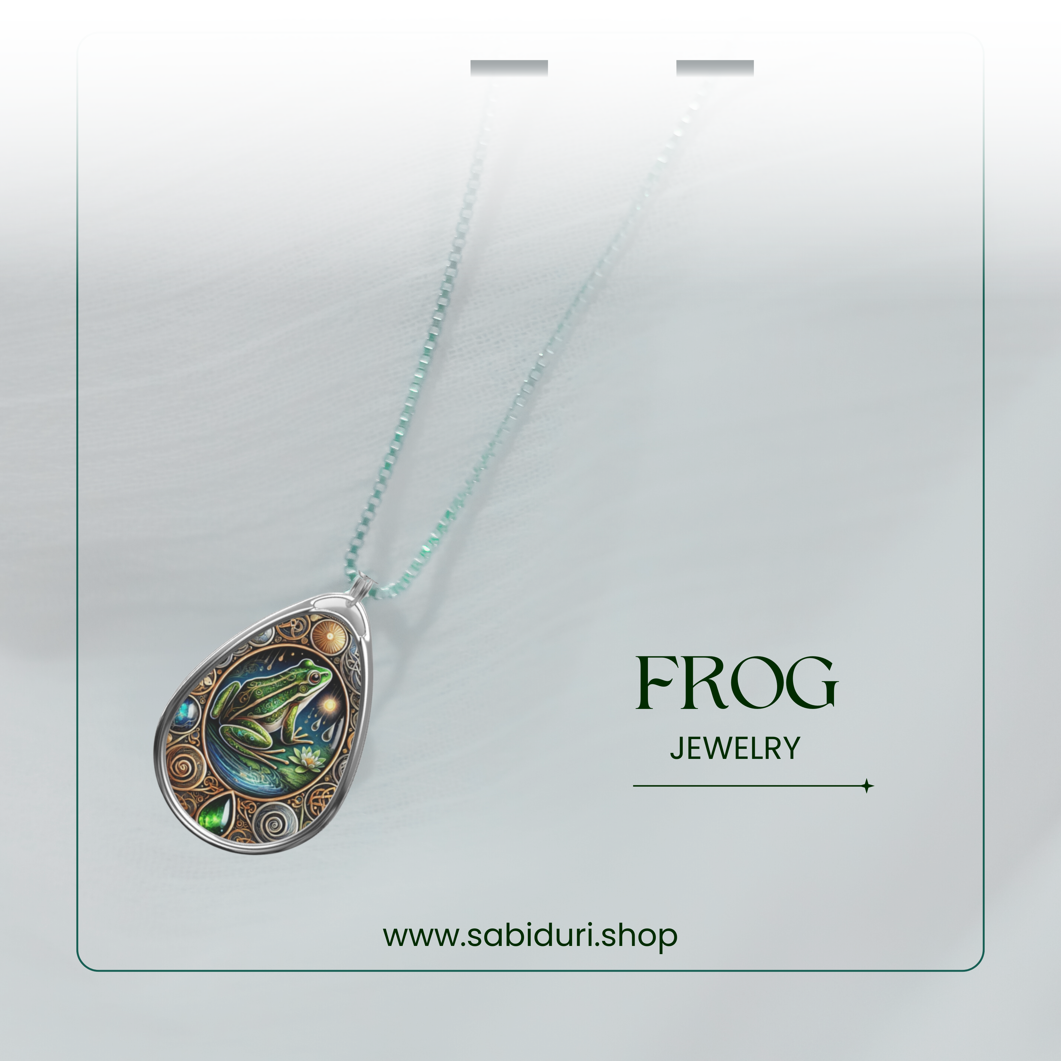  A softly lit product shot of the frog necklace, suspended against a white, textured background. The pendant’s deep greens and blues stand out, with "FROG JEWELRY" and "www.sabiduri.shop" text providing a refined branding touch.