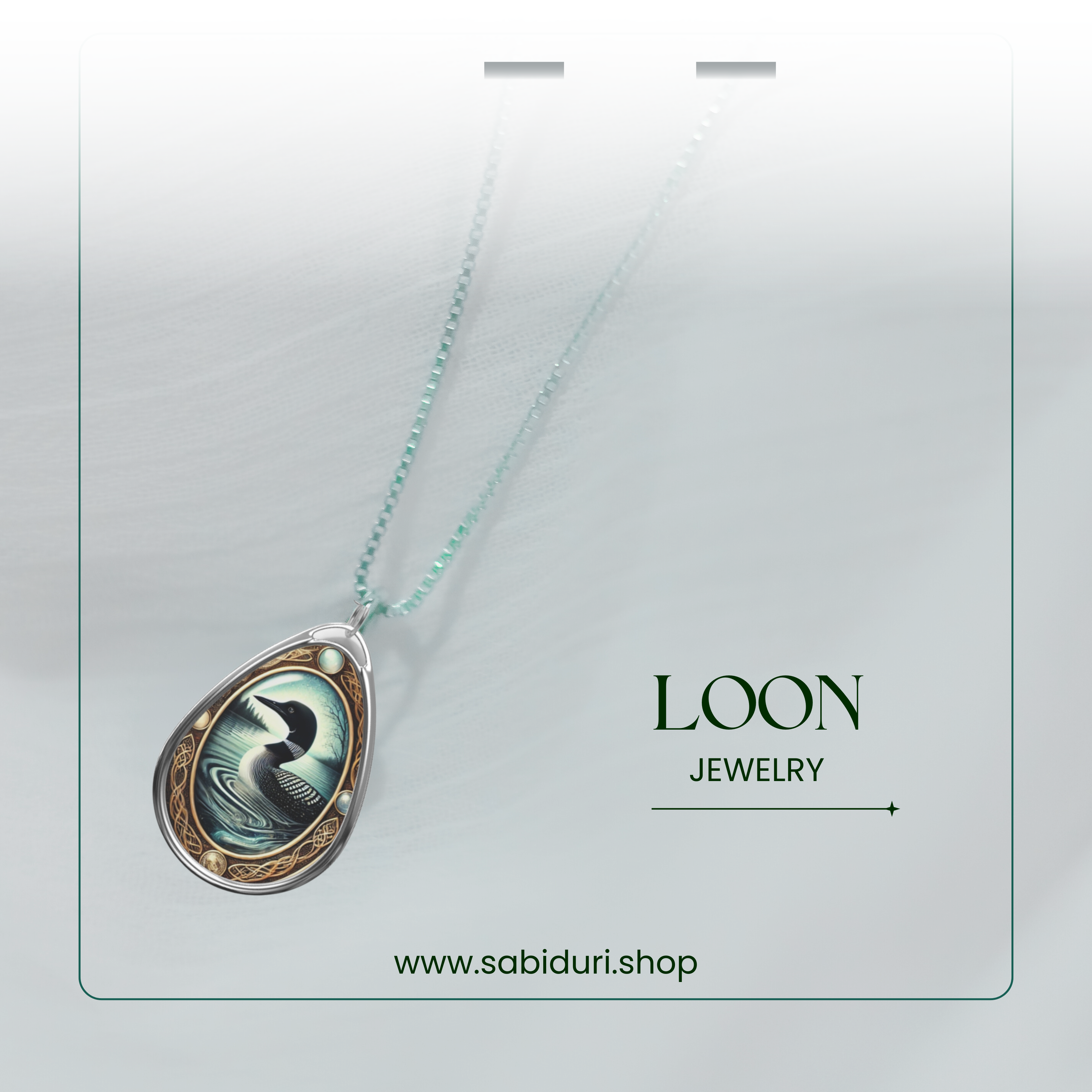 The Loon necklace is photographed against a softly lit white background, with a delicate beaded chain attached. The pendant captures the loon’s serene presence on water, surrounded by intricate golden embellishments. The text "LOON JEWELRY" and "www.sabiduri.shop" is featured in a minimalist layout.