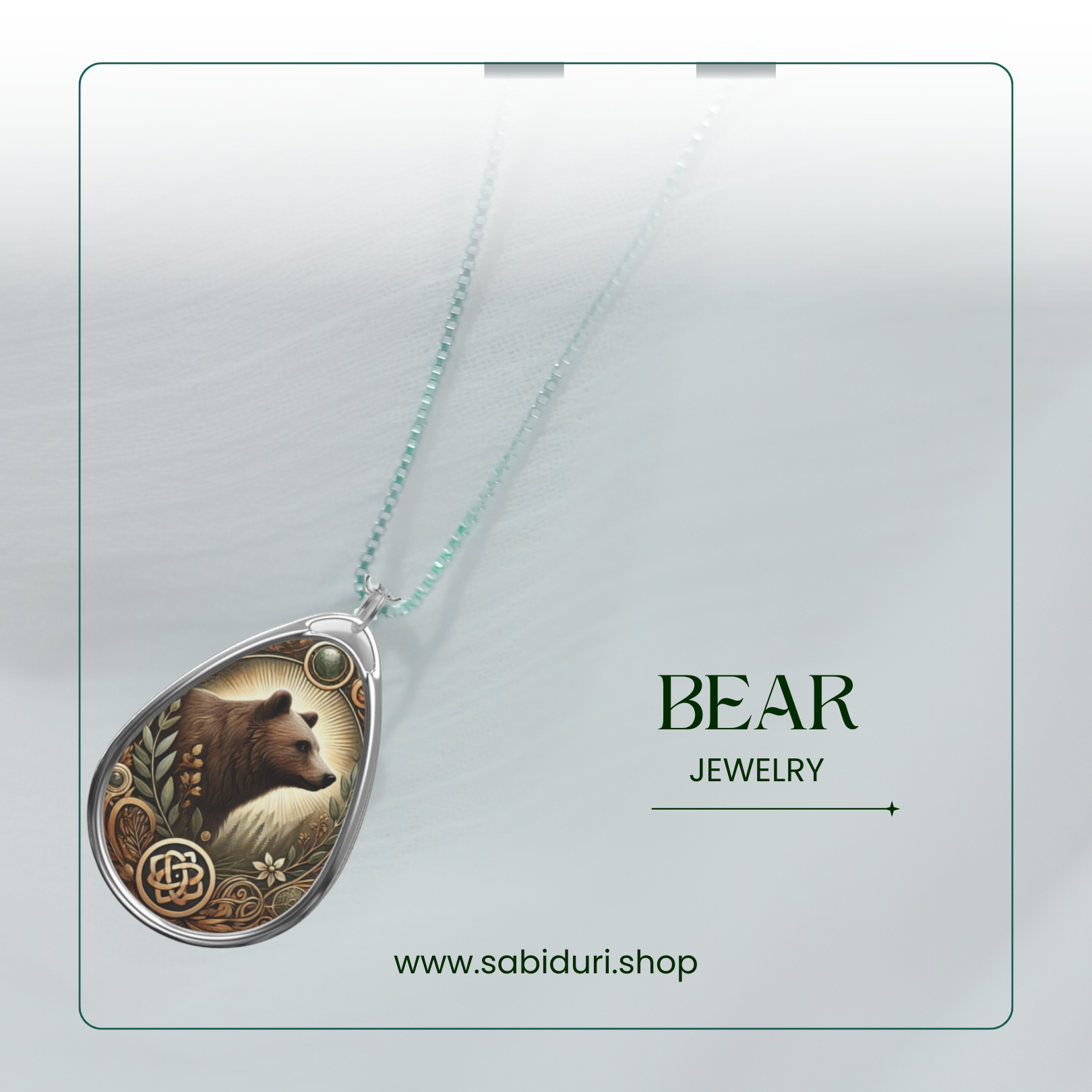 A close-up of a silver bear pendant necklace, featuring a forest-themed design with a green gemstone at the top. The pendant rests on a soft, white fabric backdrop with the words "BEAR JEWELRY" and the website "www.sabiduri.shop" in an elegant green font.