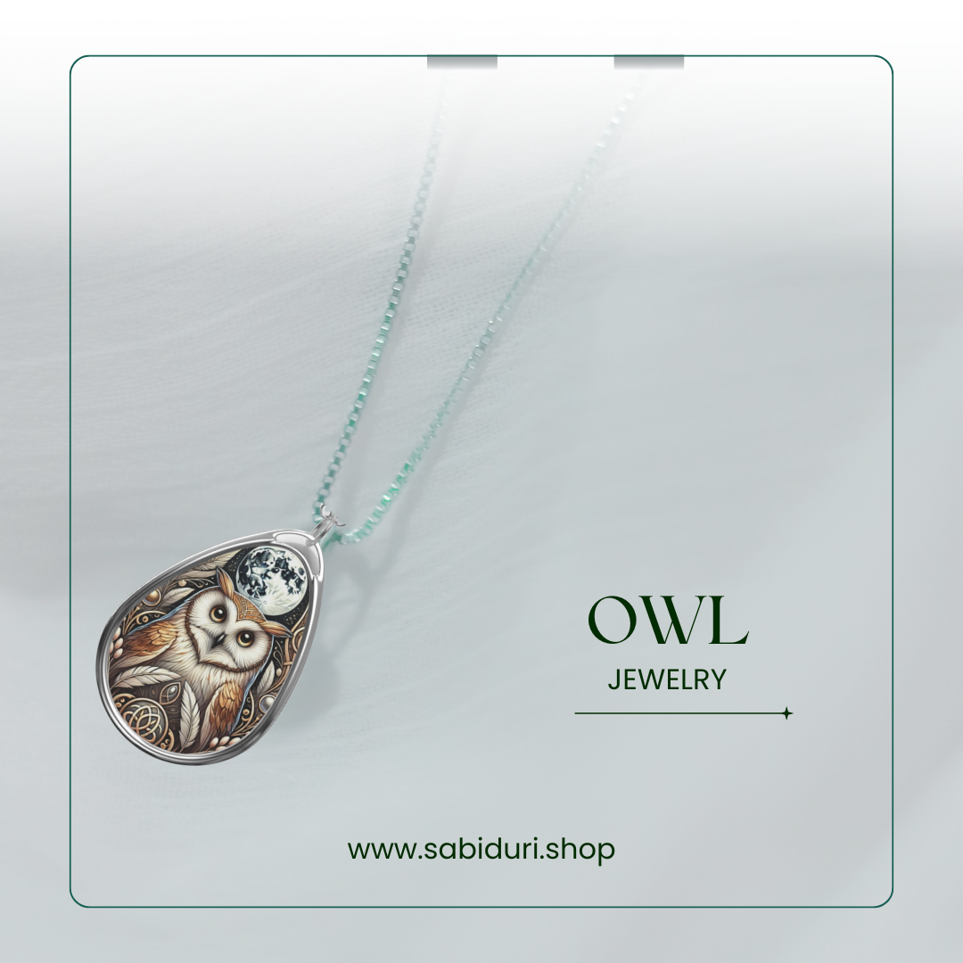 A silver owl necklace pendant placed on a soft, textured white background. The pendant features a beautifully detailed owl with a moon above its head and decorative scrollwork. The text reads "OWL Jewelry" with the website "www.sabiduri.shop" displayed at the bottom.