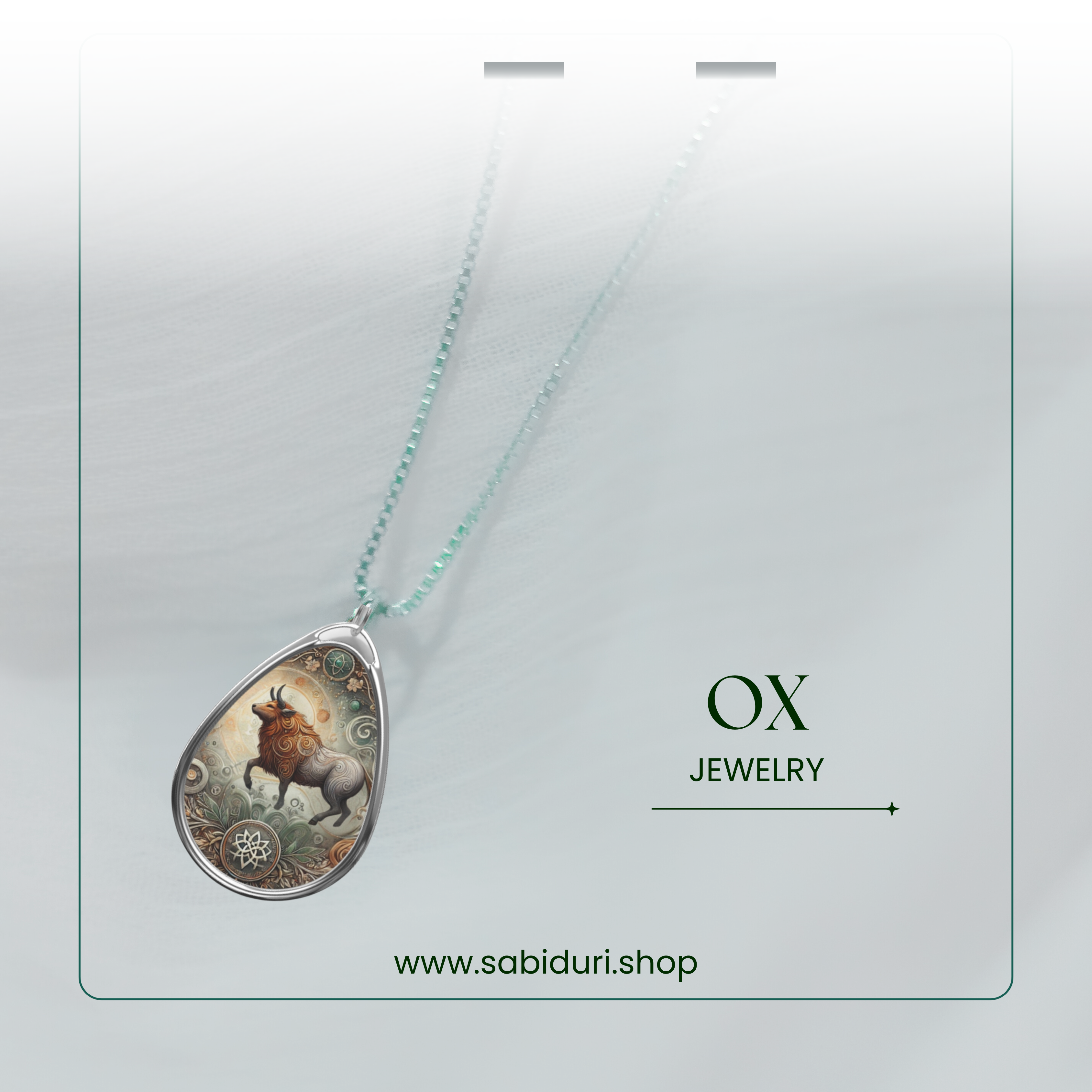 A close-up of the ox pendant hanging from a beaded silver chain, set against a soft white gradient background, with the text "Ox Jewelry" and the website "www.sabiduri.shop."