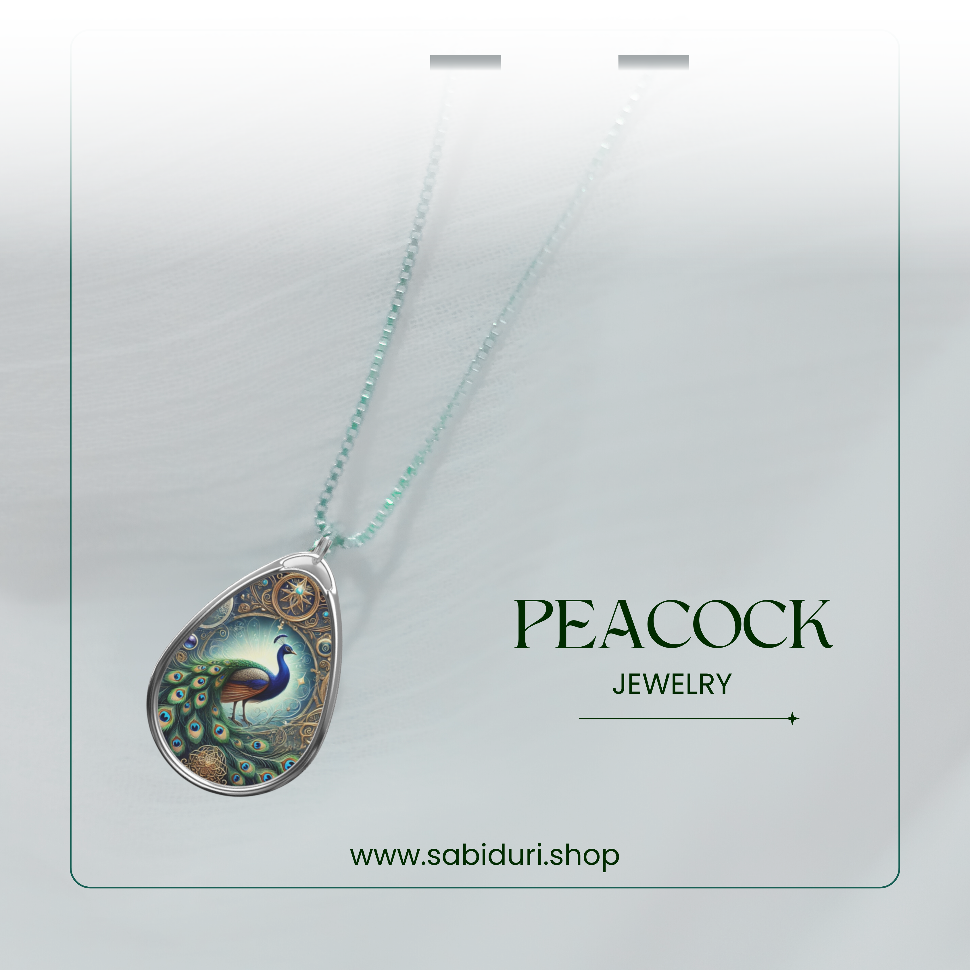 A teardrop-shaped pendant necklace featuring a detailed illustration of a vibrant peacock with an iridescent green and blue tail, surrounded by ornate gold filigree. The pendant hangs from a delicate silver chain, displayed against a soft white fabric background. The text "Peacock Jewelry" and "www.sabiduri.shop" is elegantly placed beside it.