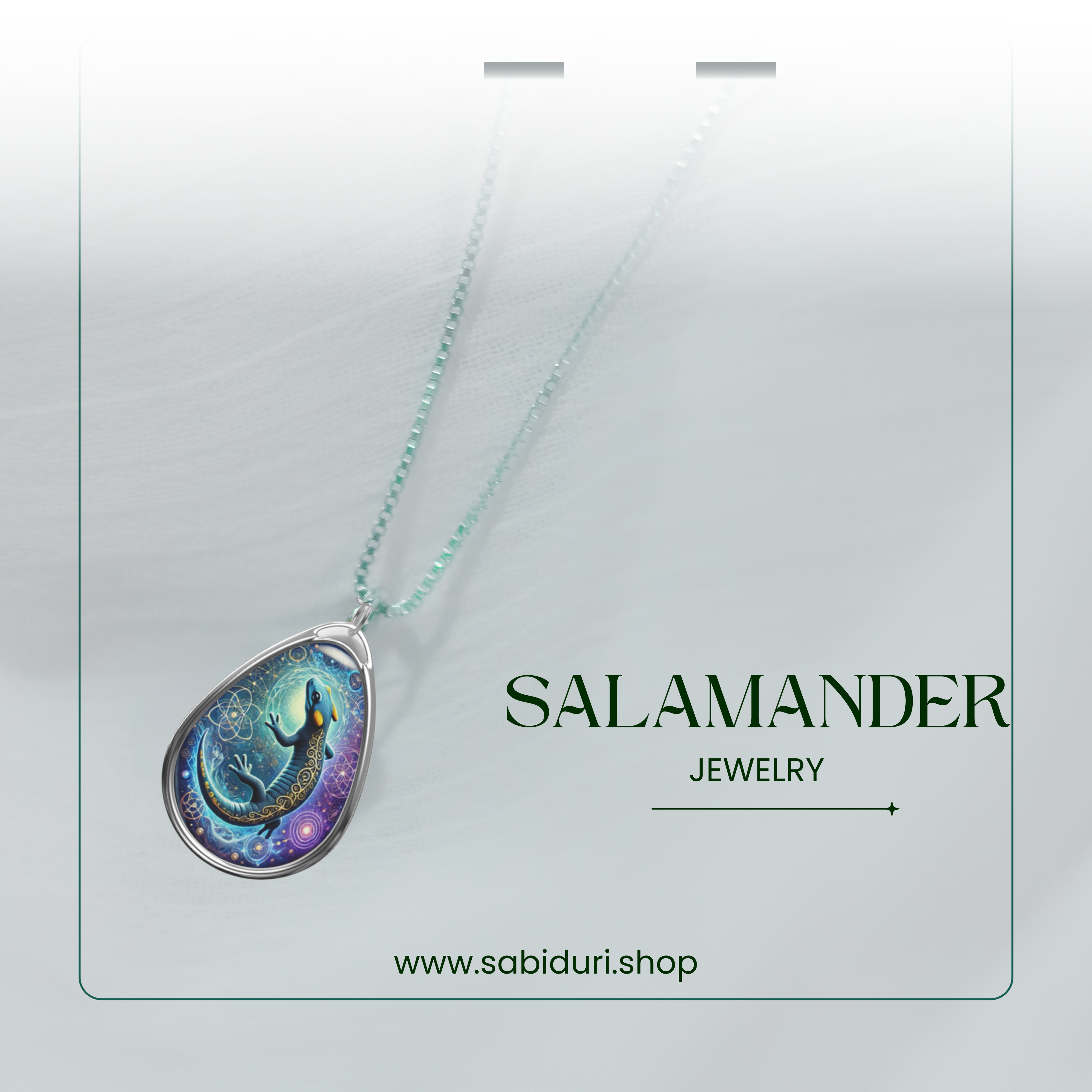 A refined presentation of a silver-chain necklace with a detailed teardrop pendant showcasing a mystical salamander design. The background is soft and blurred, featuring the text "SALAMANDER JEWELRY" and "www.sabiduri.shop."