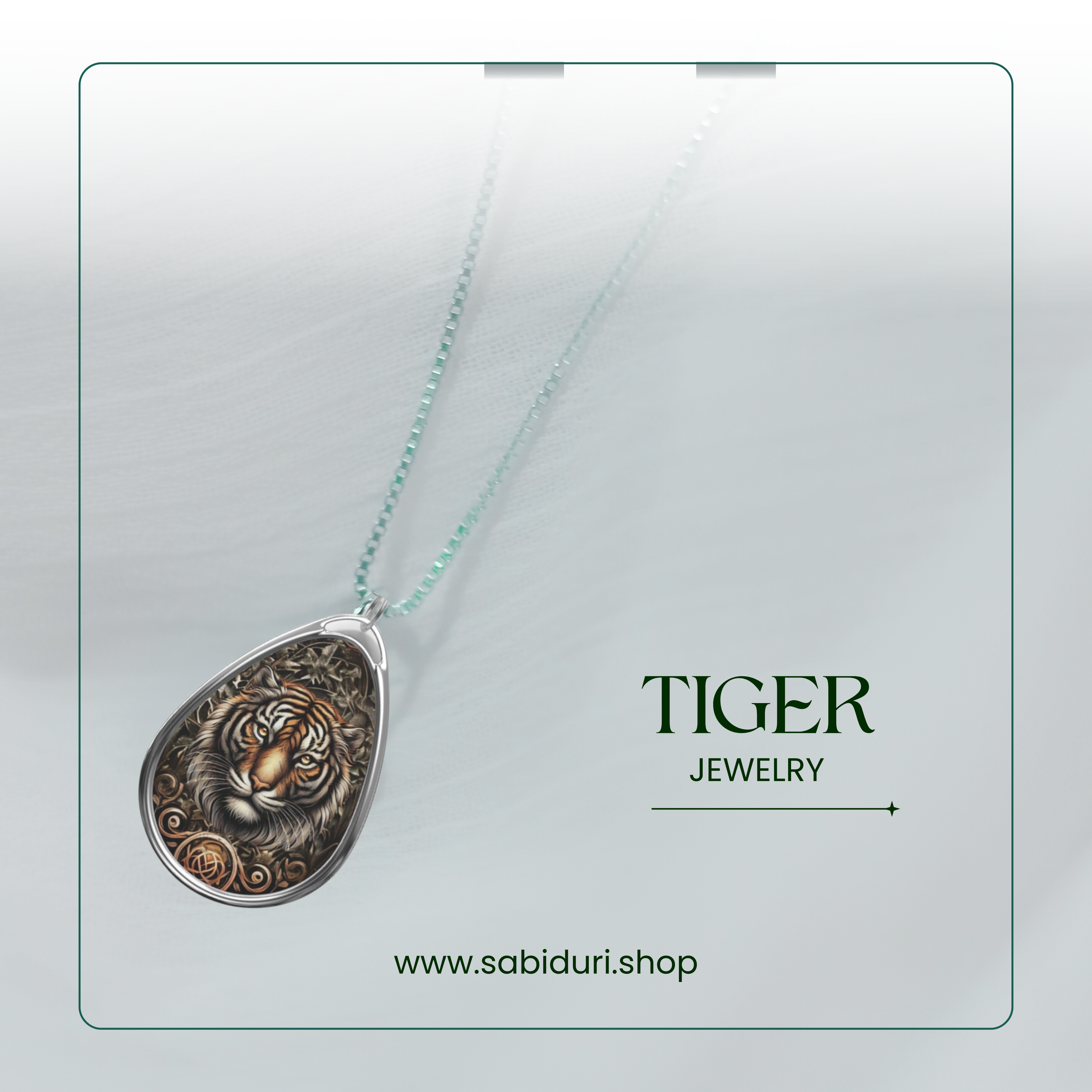 A silver necklace with a teardrop-shaped pendant featuring an intricate tiger design, displayed on a light, translucent fabric background. The word "TIGER" appears next to the pendant, followed by the word "JEWELRY" and the website URL "www.sabiduri.shop."