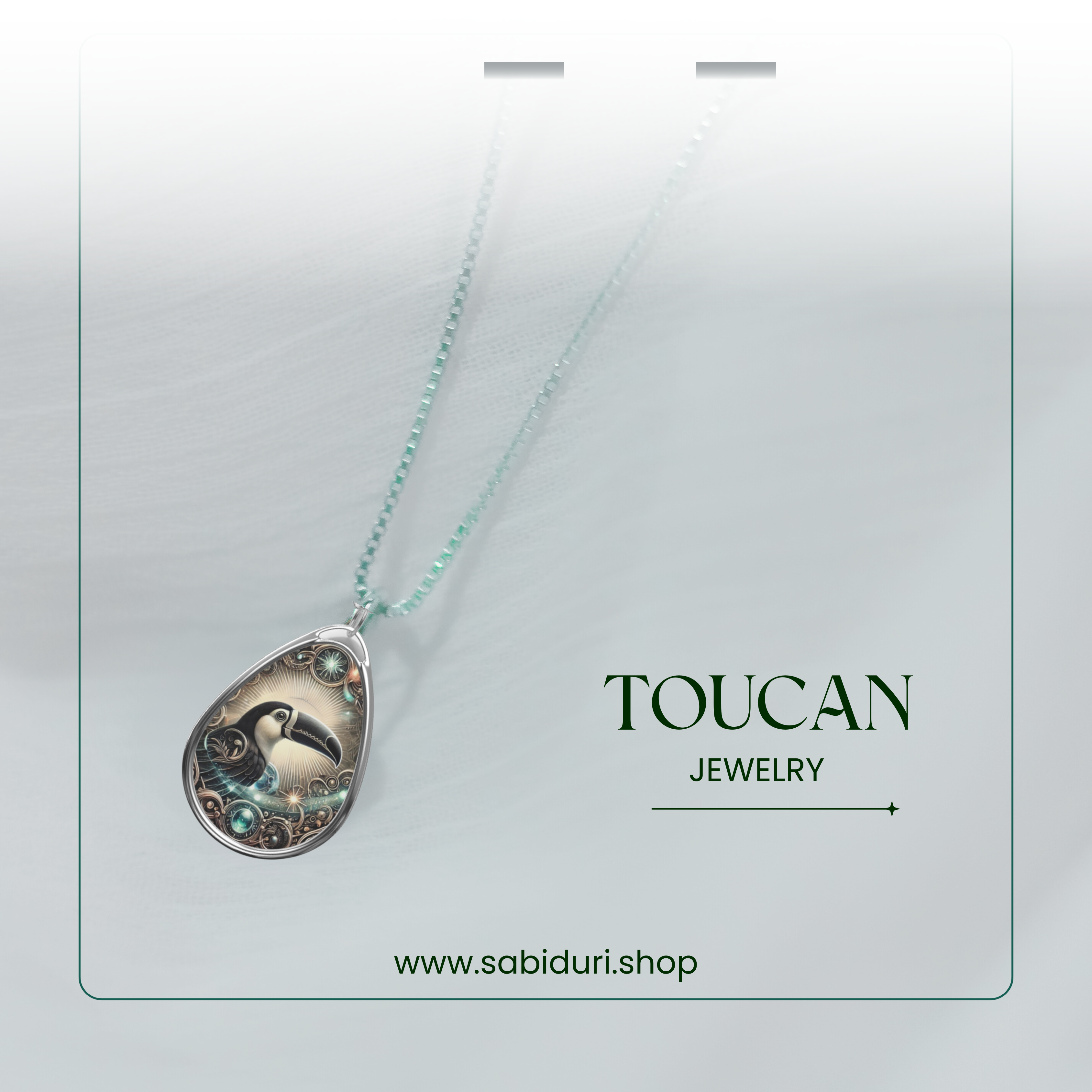 A close-up of the toucan pendant necklace on a delicate beaded chain, set against a soft white fabric background. The pendant's intricate silver details and glowing gemstones are highlighted, with "Toucan Jewelry" and the website "www.sabiduri.shop" in the lower section.