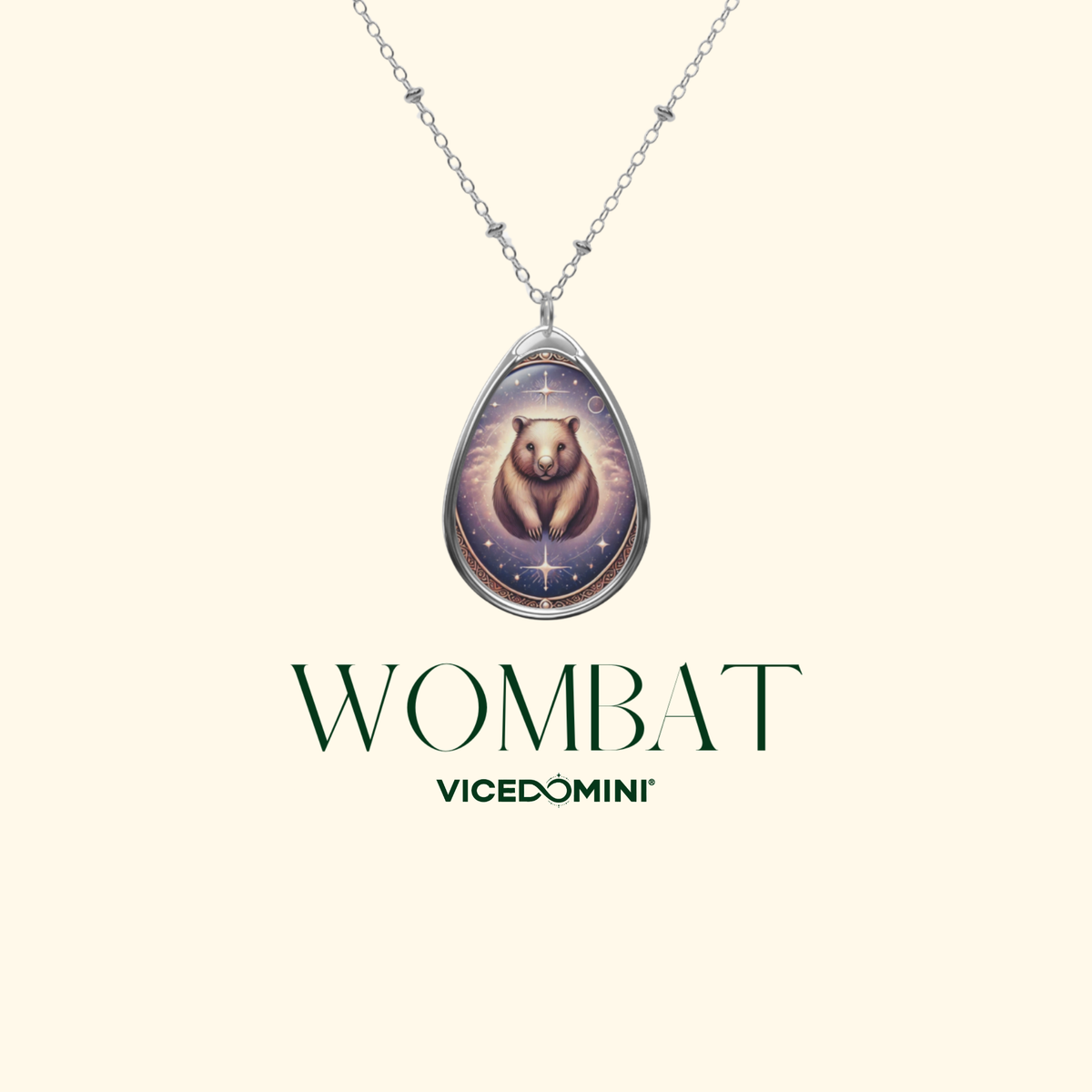A silver teardrop pendant necklace featuring a cartoon wombat illustration on a cream background, with the brand name 'WOMBAT' and 'VICEDOMINI' printed below.