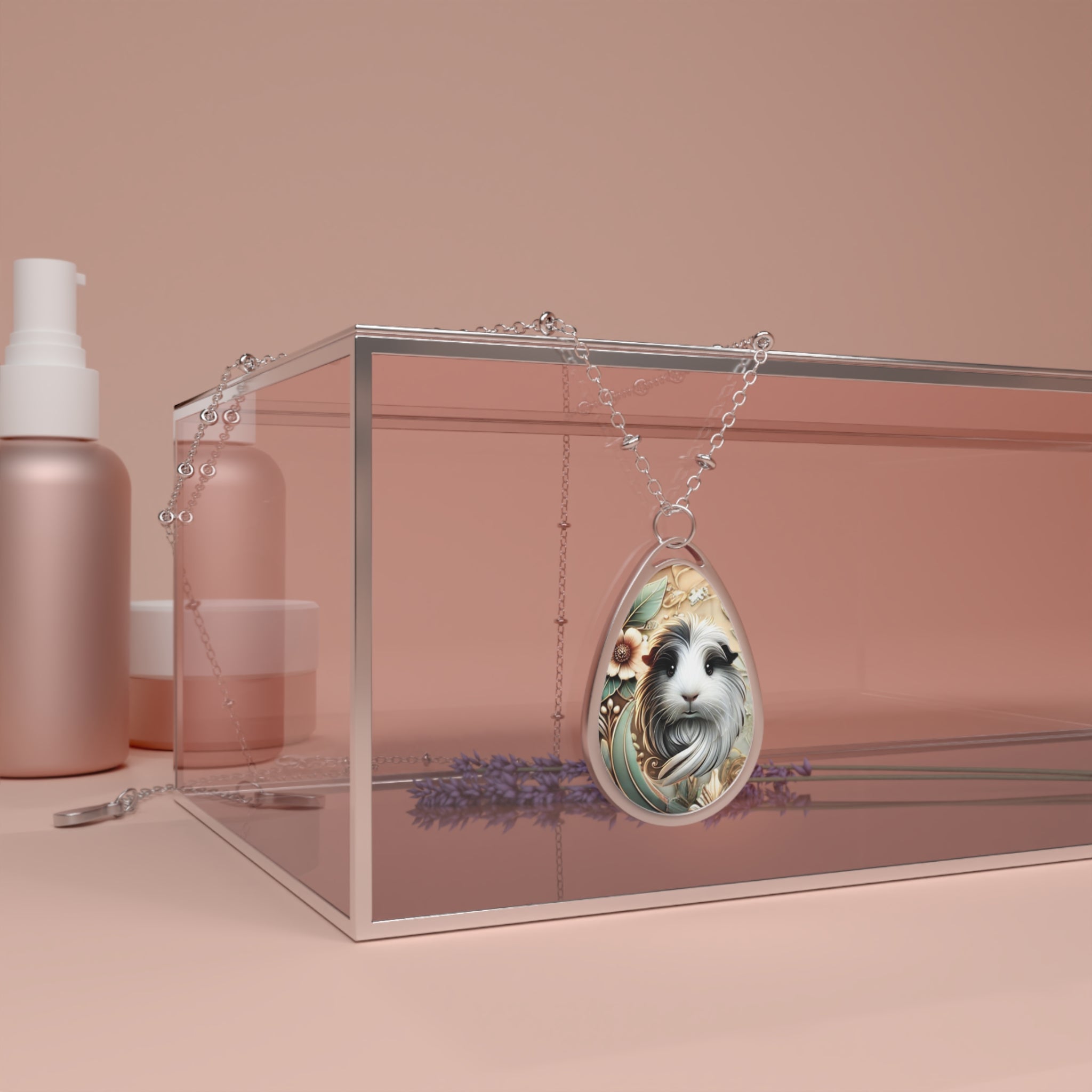 A product shot of the guinea pig necklace displayed on a clear, modern box. The silver chain is draped casually, highlighting the intricate design of the pendant featuring a guinea pig with floral accents, placed against a soft peach background with beauty products in the background.